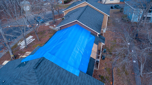 Aerial view of a home's roof partially covered with a blue tarp