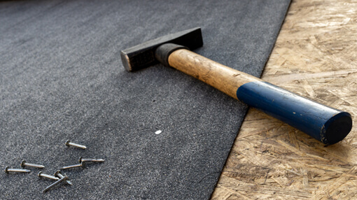 Close up of a new roof installation showing a hammer and some roofing nails